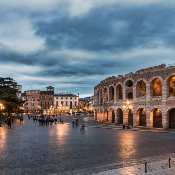 Arena de Verona iluminada al atardecer, con la Piazza Bra y gente paseando.